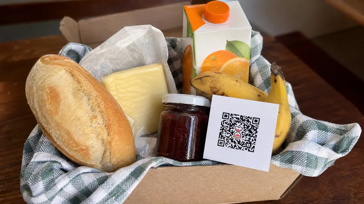 Cesta caseira com pão, queijo, geleia, suco e fruta, com cartão de QR Code apoiado no centro