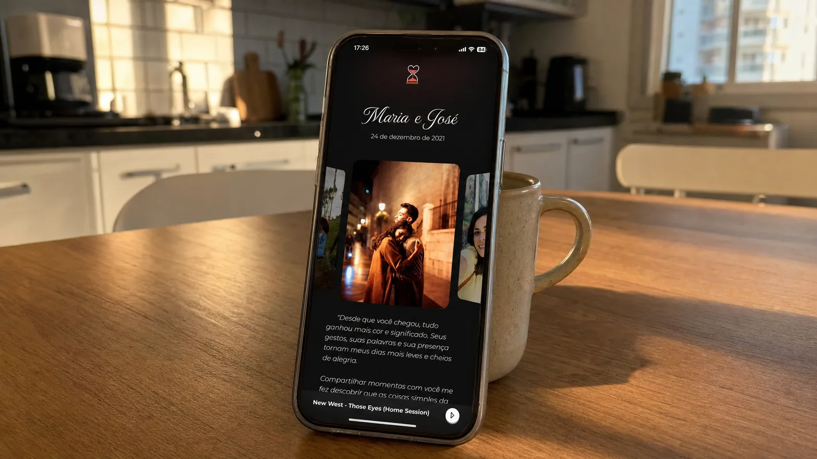 Celular apoiado na mesa exibindo um site romântico do casal com cronômetro e fotos numa cozinha simples